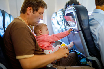 Young tired father and his crying baby daughter during flight on airplane going on vacations