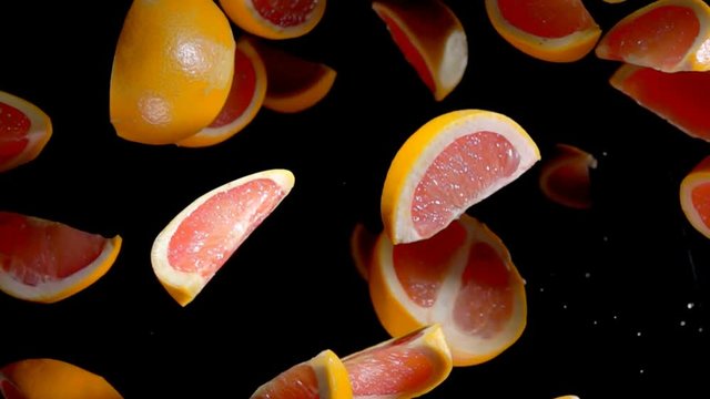 Slices of grapefruit flies to the camera on a black background in slow motion