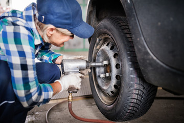 Senior female mechanic repairing a car in a garage.