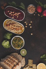Vegan food background. Vegetarian snacks: hummus, beetroot hummus, green peas dip, vegetables. Top view, dark background, copy space.