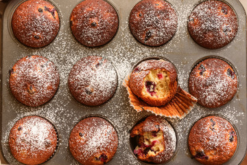 homemade muffins with forest berries one of which is bitten on a baking sheet in the oven