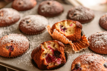 homemade muffins with forest berries one of which is bitten on a baking sheet in the oven