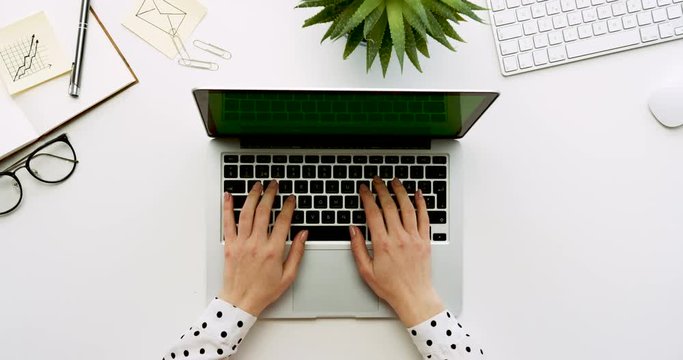 Top view on the office table with laptop computer with green screen and female hands taping on it. Office stuff beside. Chroma key.