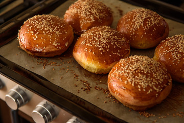 homemade burger rolls sprinkled with sesame seeds are baked in the oven