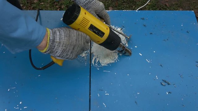 Scraping removing old blue paint from old wooden cupboard with metal scraper
