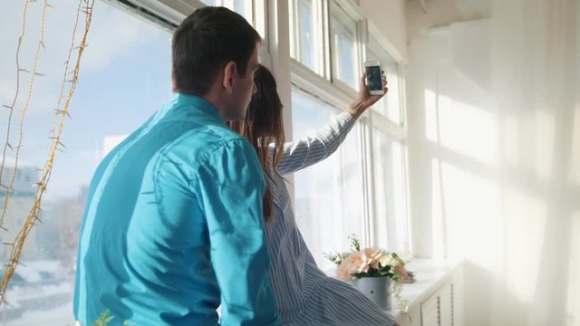 Happy cheerful loving couple making selfie on window, young attractive guy and girl