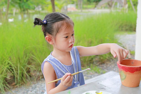 Asian kid girl paint on earthenware dish.