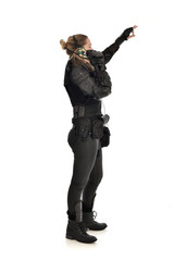 full length portrait of female  soldier wearing black  tactical armour, standing pose holding a walkie talkie, isolated on white studio background.