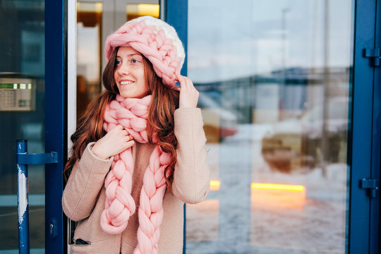 Cute young woman in knitted hat and scarf leaving the building