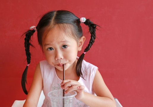 Close up little girl using straw to drink water from plastic cup in the restaurant.