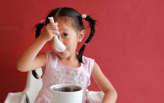 Asian child girl eating pork bone soup on high chair against red wall background at chinese restaurant.