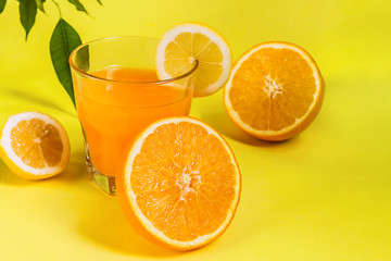 Orange juice in a glass beaker and basket with assortment of citrus fruits on a yellow background in trend style