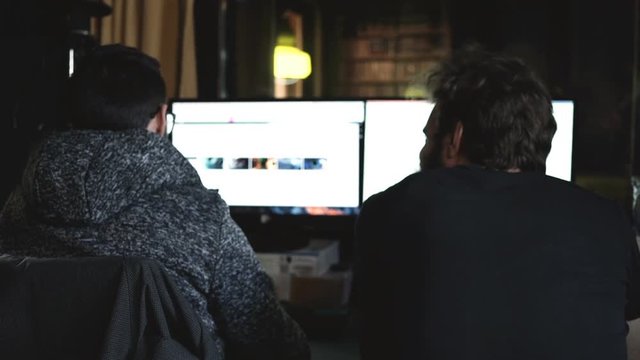 Two men at work in their office with two computer screen.