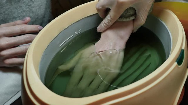 Process paraffin treatment of female hands in beauty salon.