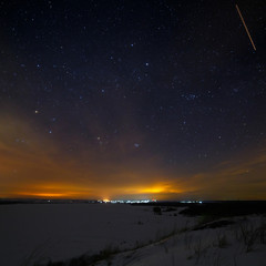 Stars of the night sky with clouds. Snowy winter landscape at dusk. The city is on the horizon.