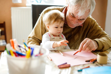 Cute little baby toddler girl and handsome senior grandfather painting with colorful pencils at...