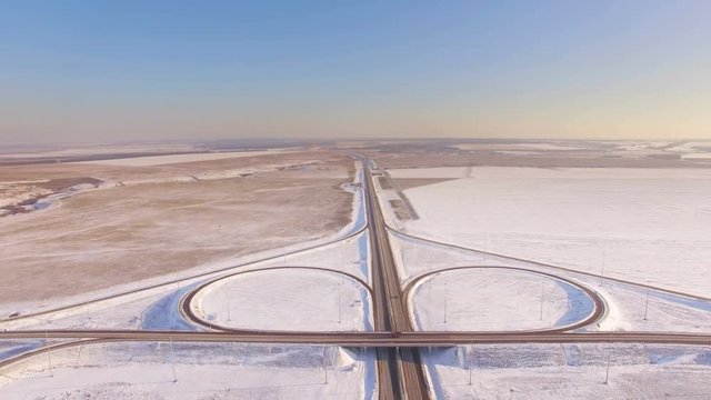 AERIAL:  View of the road junction in winter on a sunny day. Car traffic on the highway, beautiful countryside landscape.