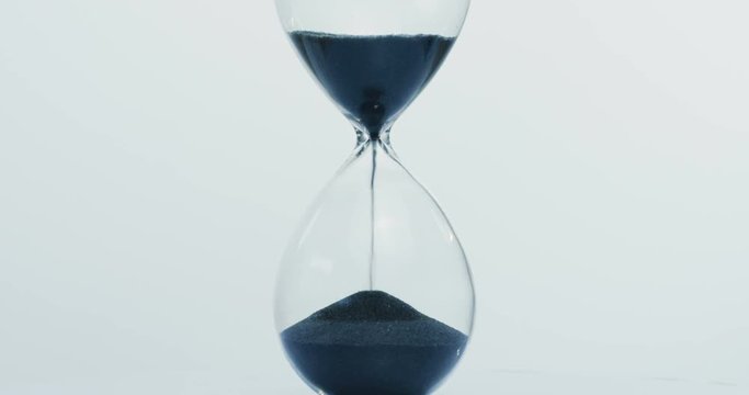 Close up of the sand clock with black sand running down on the white wall background. Macro shooting
