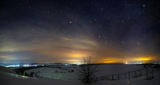 Stars of the night sky with clouds. Snowy winter landscape at dusk. Panoramic view of the valley at the hills.
