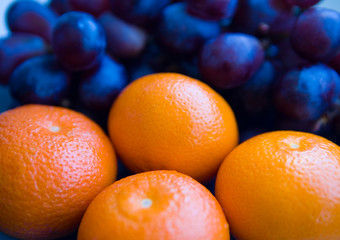Ripe mandarins and black grapes in the background.