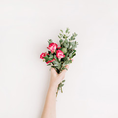 Naklejka premium Woman hand hold rose flowers and eucalyptus bouquet on white background. Flat lay, top view spring blog hero header background.