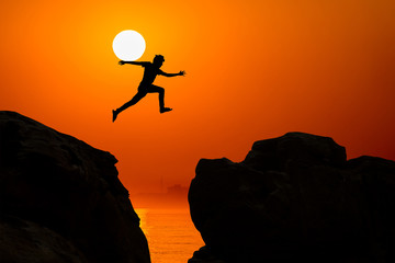 Man jumping over precipice between two rocky mountains at sunrise. Freedom, risk, challenge, success.