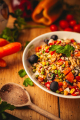 A view of a spelled dish on wooden background with some ingredients around: carrots, peppers, tomatos, parsley and oil
