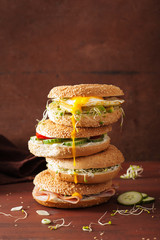 variety of sandwiches on bagels: egg, avocado, ham, tomato, soft cheese, alfalfa sprouts