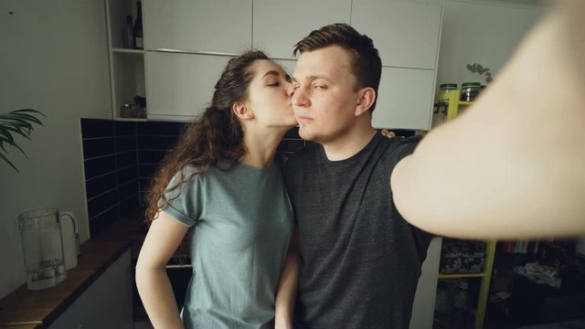 POV of Young funny couple taking selfie photos with smartphone camera standing in the kitchen at home in the morning