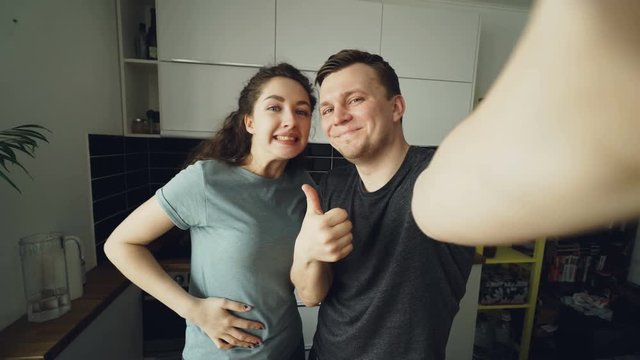 POV of Young funny couple taking selfie photos with smartphone camera standing in the kitchen at home in the morning