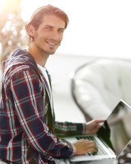 stylish young man working on laptop and looking at camera