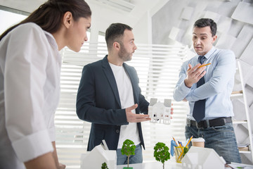 Seriousness. Attractive concentrated young dark-haired man holding a pencil and discussing a project with his colleagues while sitting at the table