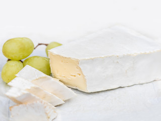  Brie cheese with slices and grape on white, close up.  