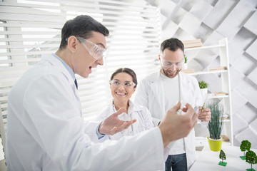 Great results. Cheerful professional experienced scientists smiling and wearing uniforms and holding test tubes