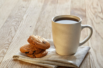 Porcelain teacup with chocolate chips cookies on cotton napkin on a rustic wooden background, top view