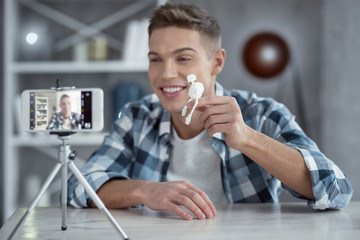 My new hobby. Attractive exuberant young well-built man smiling and holding a little skeleton in his hand while making a video