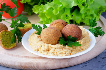 Falafel balls and bowl with hummus on light cutting board. Close-up view.
