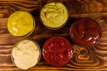 Different sauces in glass bowls on wooden table. Top view
