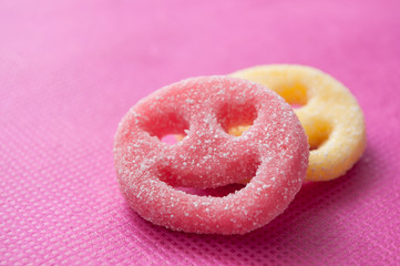 closeup of acidulous candies in shaped smiley on pink background