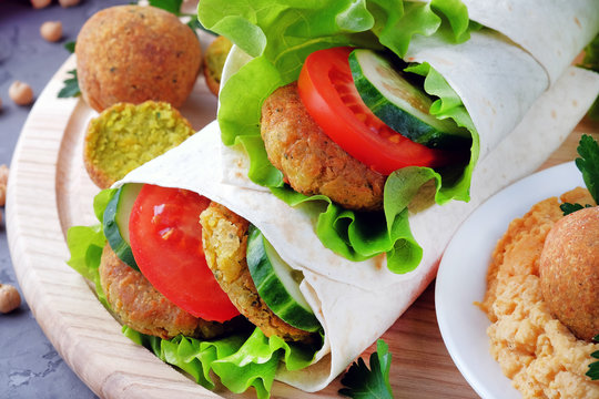 Falafel and vegetables wrapped in lavash on a light cutting board. Vegetarian and vegan food. Close-up view.