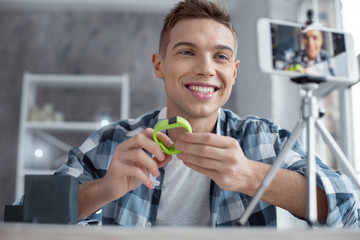 My fitness bracelet. Handsome content well-built blogger holding his bracelet and smiling while making a video