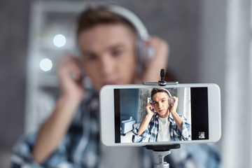 Relaxation. Good-looking joyful professional well-built blogger wearing his headphones and relaxing while making a video