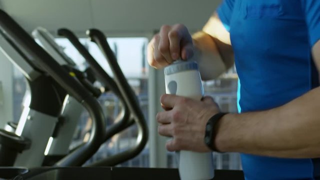 Close up side view shot of man running on treadmill at the gym, taking bottle and drinking water from it