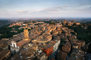 Fototapeta na wymiar Picturesque aerial view of typical buildings red roofs from above at sunset from Torre del Mangia tower, Tuscany, Italy. Travel destination colorful golden hour postcard.