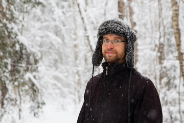 Man in fur winter hat with ear flaps smiling portrait. Extreme in the forest