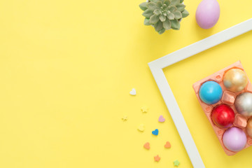 Flat lay top view colorful easter egg painted in pastel colors composition and spring flowers on yellow pastel color background. Easter day background top view with copy space.