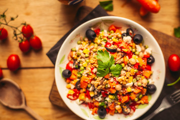 A view of a spelled dish on wooden background with some ingredients around: carrots, peppers, tomatos, parsley and oil
