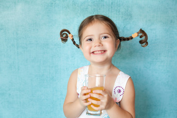 Smiling girl with funny pigtails with glass of juice