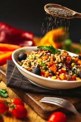 A view of a spelled dish on wooden background with some ingredients around: carrots, peppers, tomatos, parsley and oil