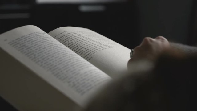 Girl finishes a chapter of a very big book placed on her legs.